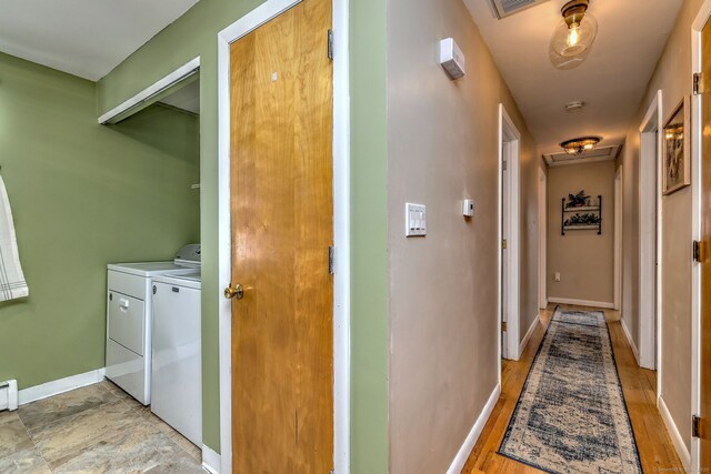 corridor with a baseboard heating unit, attic access, baseboards, and washing machine and clothes dryer