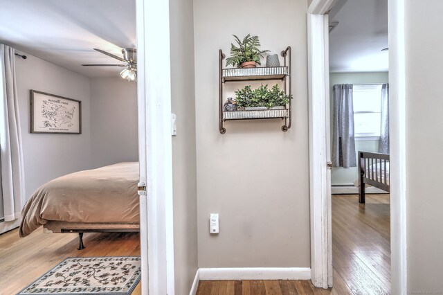 bedroom with a baseboard heating unit, baseboards, and wood finished floors