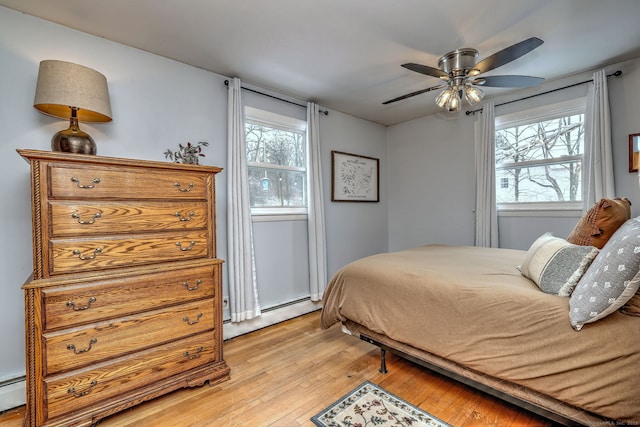 bedroom featuring light wood finished floors, ceiling fan, and a baseboard heating unit