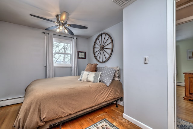 bedroom featuring a baseboard heating unit, visible vents, ceiling fan, and wood finished floors