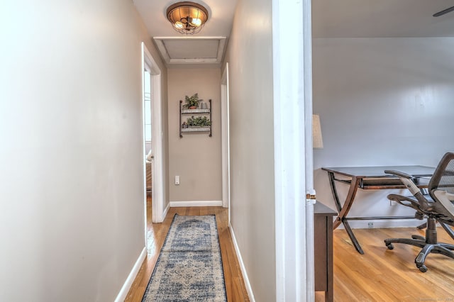 hall with baseboards, attic access, and light wood-style floors