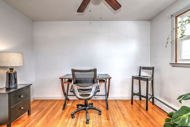 office area with a ceiling fan, a baseboard radiator, light wood-style flooring, and baseboards