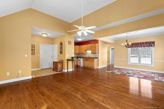 unfurnished living room featuring lofted ceiling, light wood-style flooring, ceiling fan with notable chandelier, a sink, and baseboards