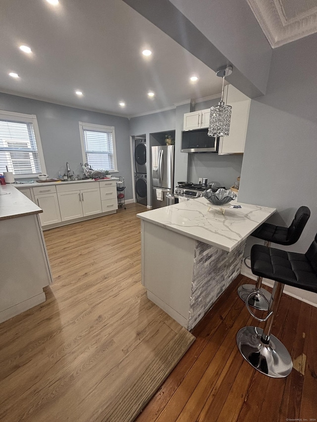 kitchen with stacked washer and dryer, a kitchen breakfast bar, stainless steel appliances, white cabinetry, and pendant lighting