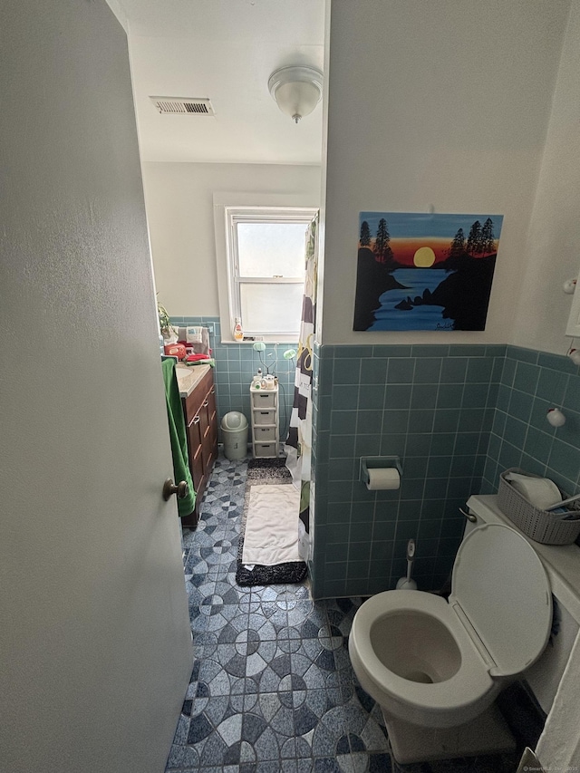 full bathroom featuring toilet, visible vents, a wainscoted wall, and tile walls