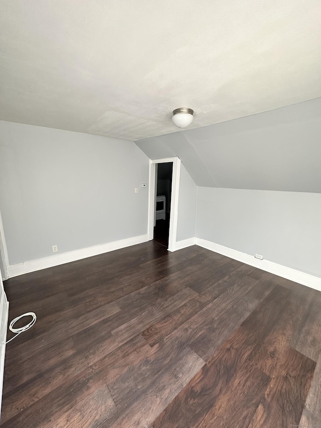 additional living space featuring vaulted ceiling, dark wood finished floors, and baseboards