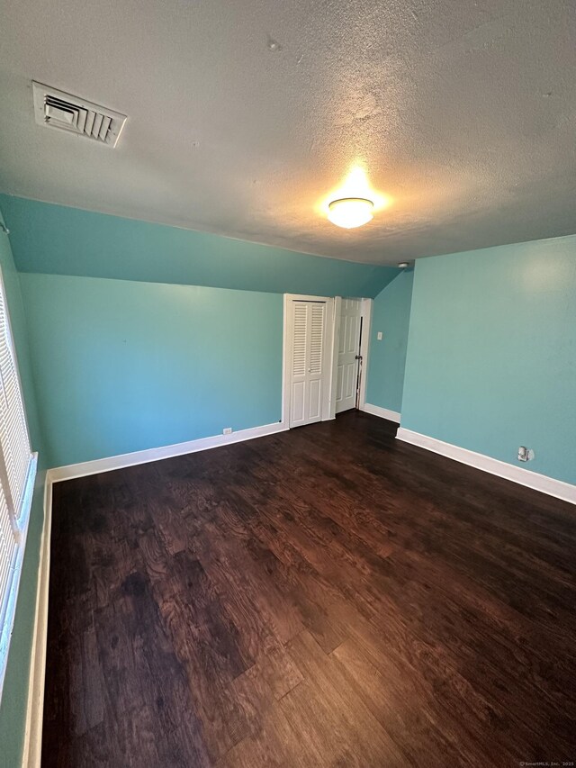 unfurnished bedroom with baseboards, visible vents, dark wood-style floors, a textured ceiling, and a closet