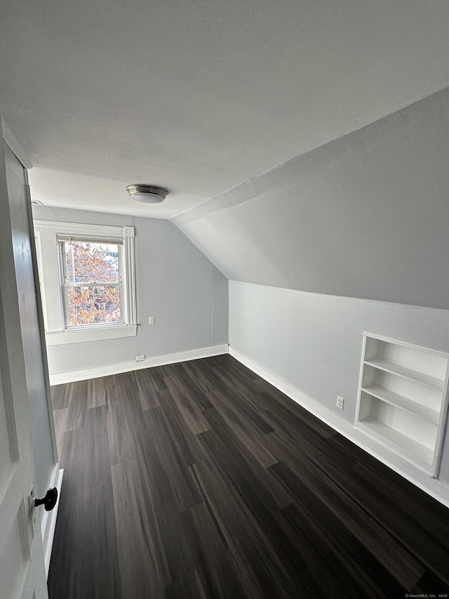 bonus room featuring lofted ceiling, built in shelves, dark wood-style flooring, and baseboards