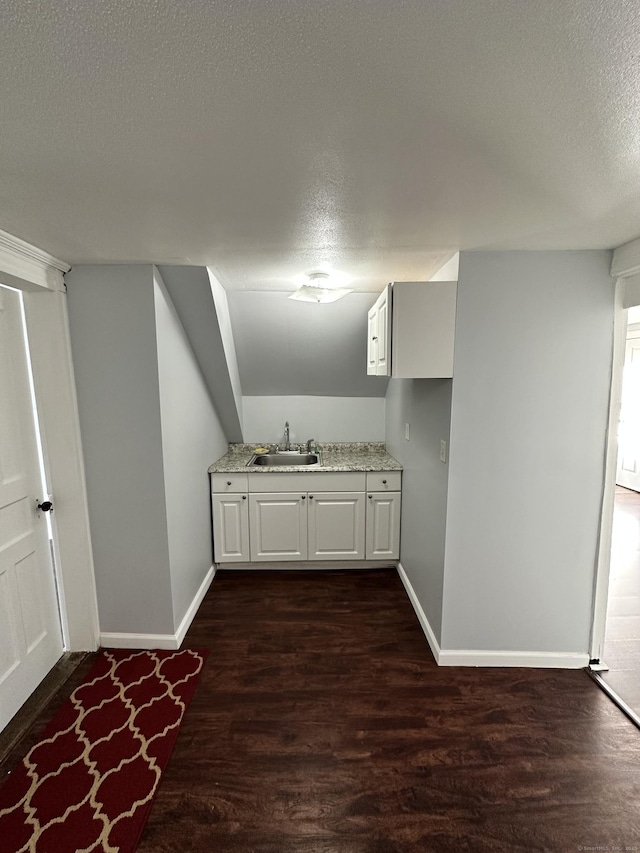 bar featuring a sink, a textured ceiling, dark wood finished floors, and baseboards