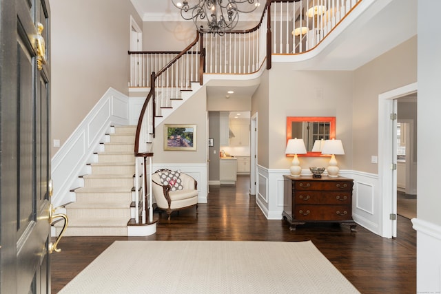 entrance foyer featuring stairway, dark wood-type flooring, crown molding, a chandelier, and a decorative wall