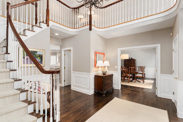 entrance foyer featuring a wainscoted wall, stairway, dark wood-type flooring, and a notable chandelier