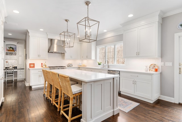 kitchen featuring white cabinets, a center island, hanging light fixtures, light countertops, and wall chimney range hood