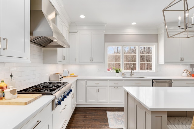 kitchen with light countertops, appliances with stainless steel finishes, white cabinets, a sink, and wall chimney range hood