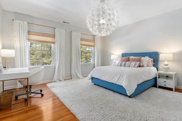 bedroom featuring a notable chandelier, visible vents, baseboards, and wood finished floors