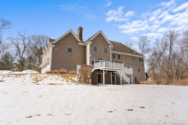 snow covered back of property featuring stairway, a chimney, and a wooden deck