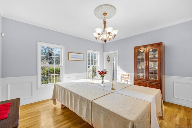 dining area featuring a chandelier, wainscoting, crown molding, and light wood-style flooring