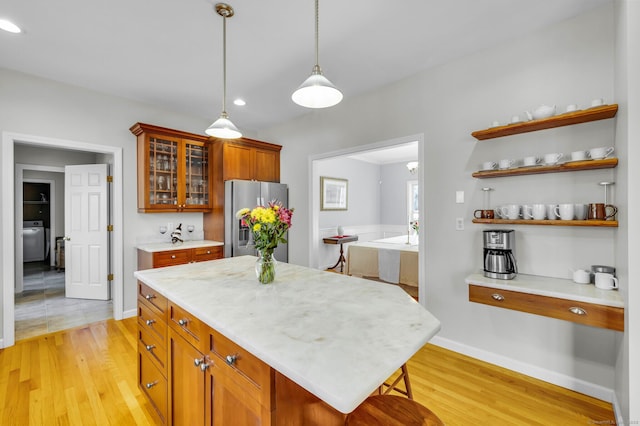 kitchen featuring light wood-style floors, hanging light fixtures, stainless steel fridge with ice dispenser, brown cabinetry, and glass insert cabinets