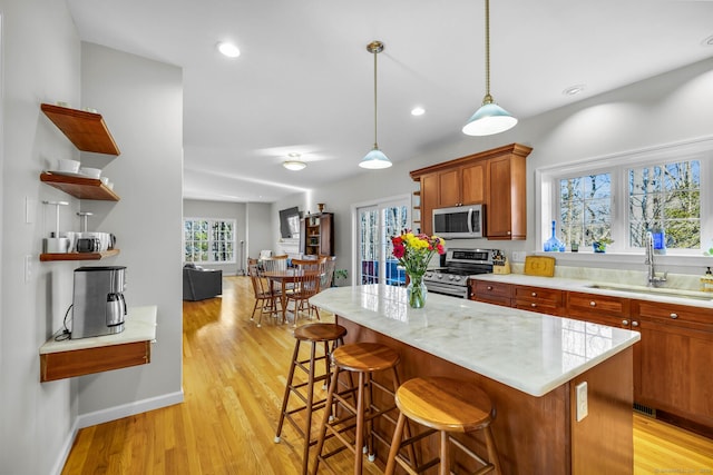 kitchen featuring a sink, light wood-style floors, appliances with stainless steel finishes, open shelves, and decorative light fixtures