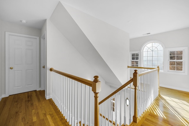 corridor with baseboards, visible vents, an upstairs landing, and wood finished floors