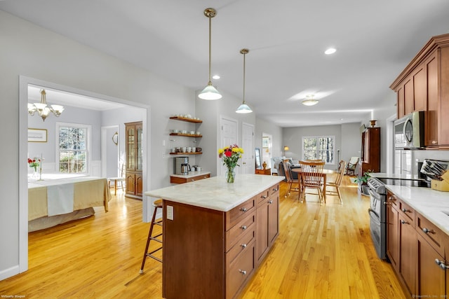 kitchen with hanging light fixtures, light wood-style floors, appliances with stainless steel finishes, and a breakfast bar area