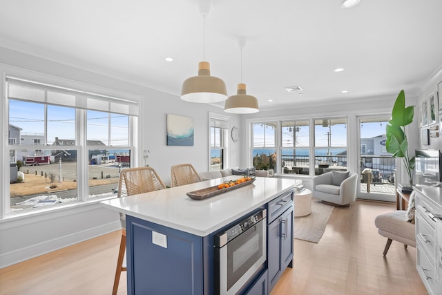 kitchen featuring white cabinets, stainless steel microwave, light countertops, a kitchen bar, and pendant lighting