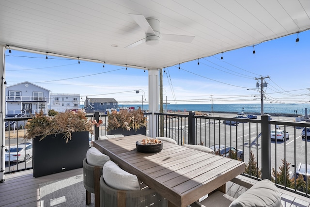 deck with outdoor dining area, a water view, and a ceiling fan