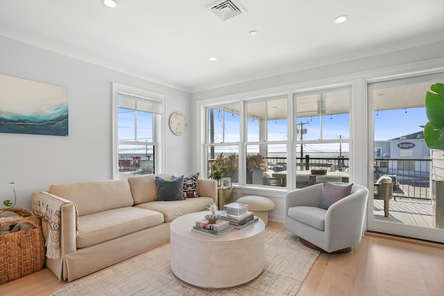 living room featuring a healthy amount of sunlight, light wood-style floors, visible vents, and ornamental molding