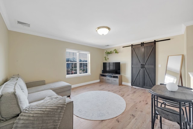 living room with a barn door, light wood-style flooring, visible vents, baseboards, and ornamental molding