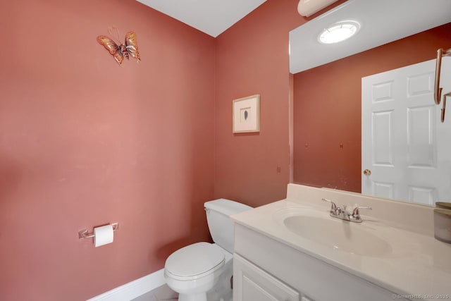 half bath featuring baseboards, vanity, and toilet