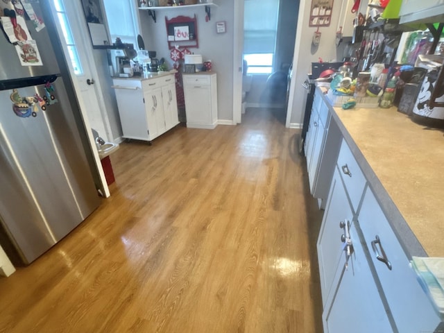 kitchen with light wood-type flooring, freestanding refrigerator, light countertops, and white cabinetry