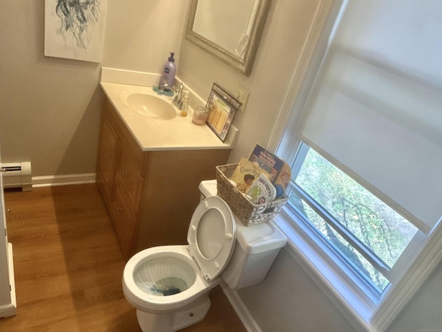 half bath with baseboard heating, toilet, vanity, wood finished floors, and baseboards