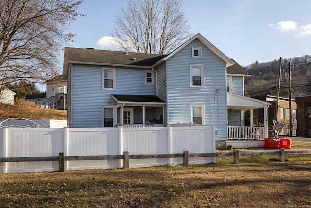 back of property with a porch, a yard, and fence