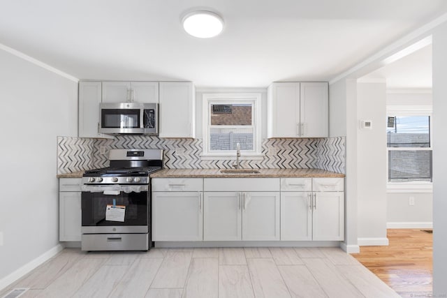 kitchen with baseboards, appliances with stainless steel finishes, a sink, crown molding, and backsplash