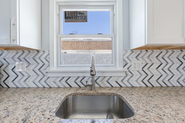 room details with white cabinets, light stone counters, backsplash, and a sink