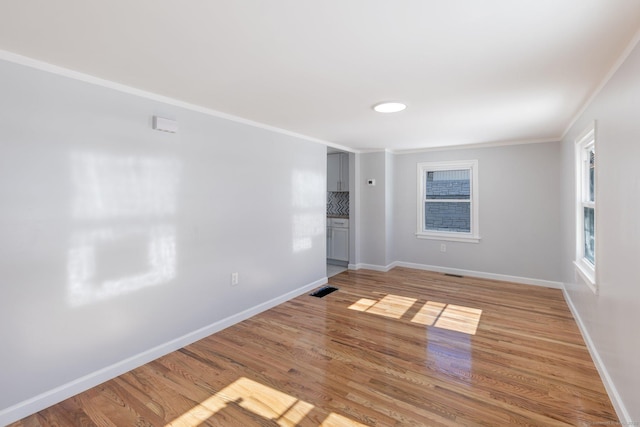 empty room featuring visible vents, crown molding, baseboards, and wood finished floors