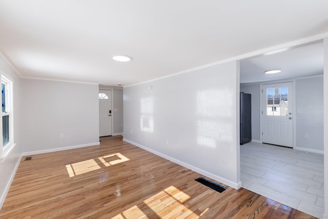 spare room with light wood-type flooring, visible vents, baseboards, and crown molding