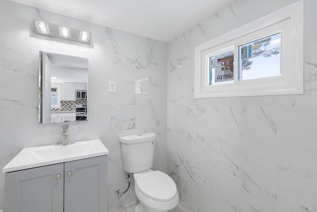 half bath featuring toilet, marble finish floor, and vanity