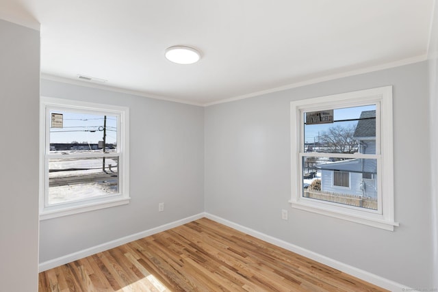 empty room featuring visible vents, ornamental molding, light wood-style flooring, and baseboards