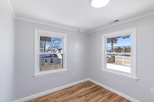 empty room featuring visible vents, crown molding, baseboards, and wood finished floors