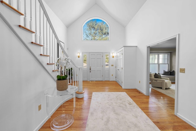 foyer entrance with high vaulted ceiling, stairway, baseboards, and wood finished floors