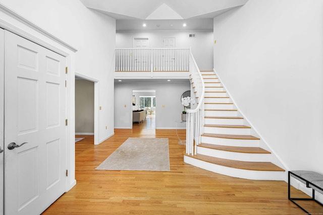 stairs featuring a towering ceiling, baseboards, wood finished floors, and recessed lighting