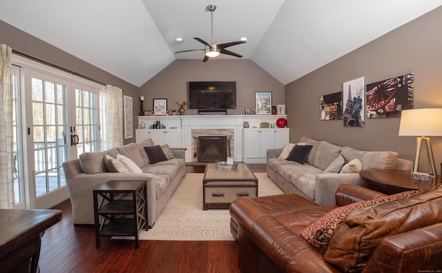 living room featuring dark wood finished floors, lofted ceiling, a stone fireplace, and a ceiling fan