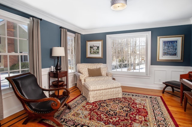 sitting room featuring a wainscoted wall, wood finished floors, crown molding, and a decorative wall