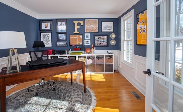 office space featuring a wainscoted wall, wood finished floors, visible vents, and ornamental molding