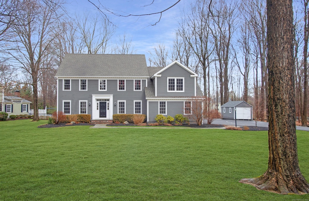 view of front of property featuring an outbuilding, a front lawn, and a shingled roof