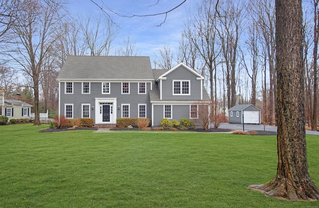 view of front of property featuring an outbuilding, a front lawn, and a shingled roof