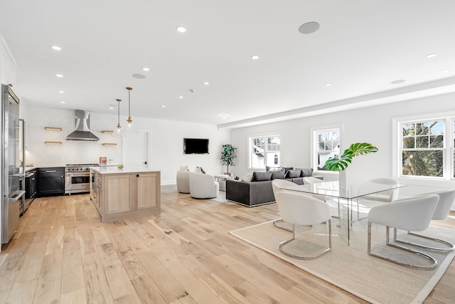 kitchen with recessed lighting, light wood-style flooring, open floor plan, wall chimney range hood, and high end range