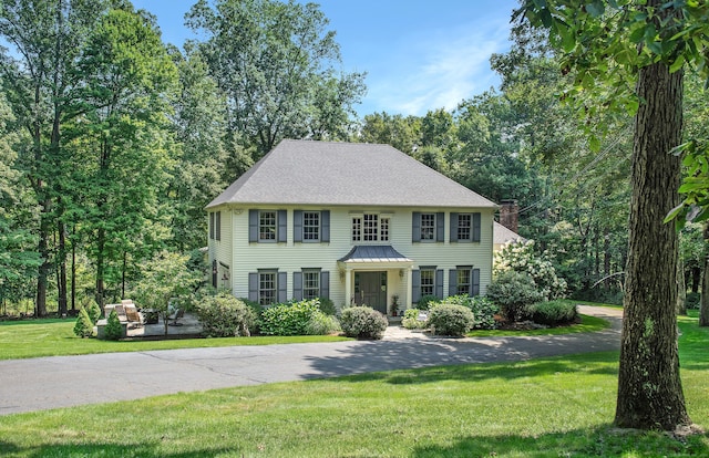 colonial home featuring roof with shingles and a front yard