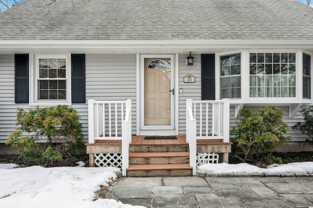 snow covered property entrance featuring a shingled roof