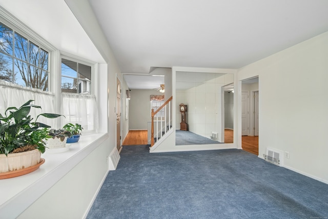 empty room with stairs, dark carpet, visible vents, and baseboards